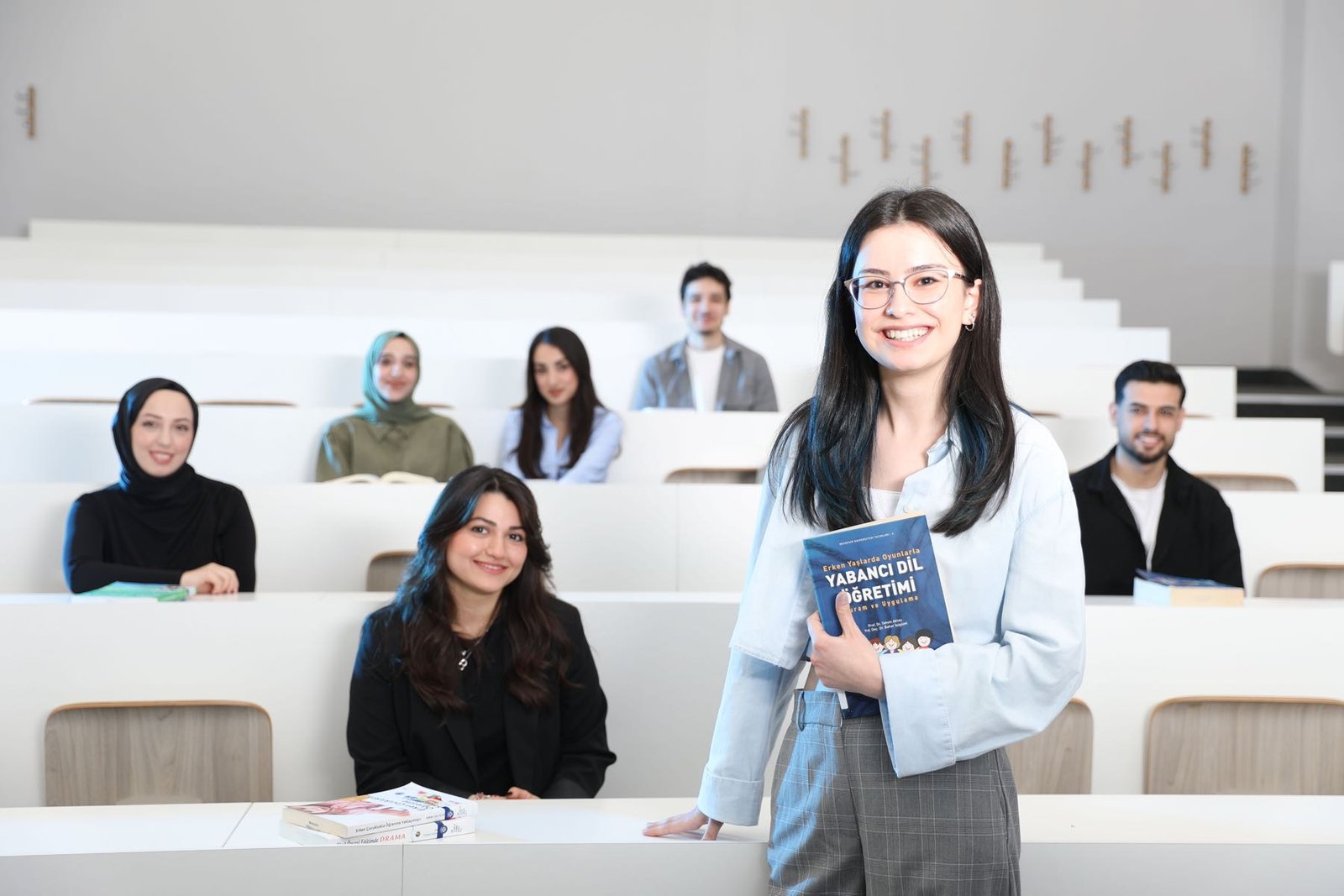 University students smiling with a language-teaching textbook in a lecture hall